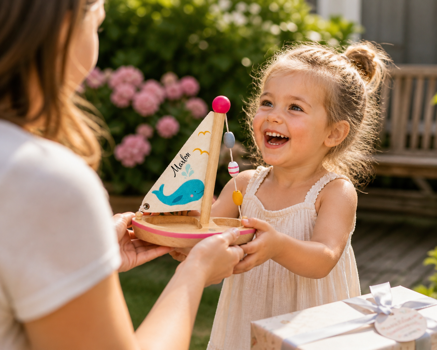 Glückliches Kind nimmt personalisiertes Holzspielzeug Segelboot als Geschenk entgegen – liebevolle Geschenkidee für Kinder mit Namen