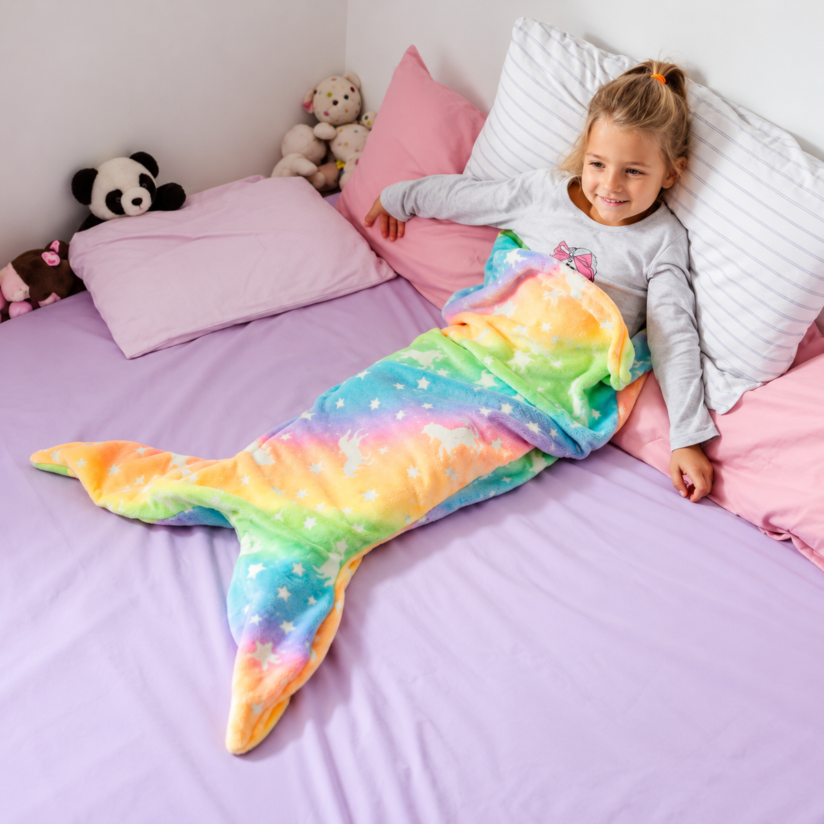 Kind kuschelt auf dem Bett in einer regenbogenfarbenen Meerjungfrauen-Decke